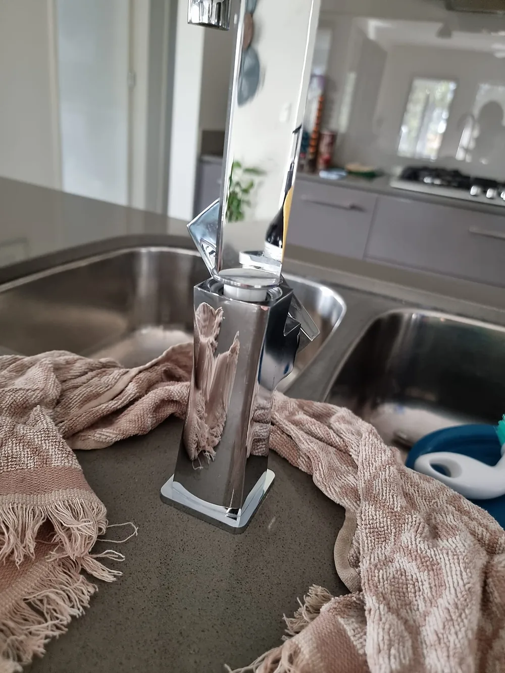 Chrome kitchen mixer on a benchtop after its spout popped out, towels soaking up the water